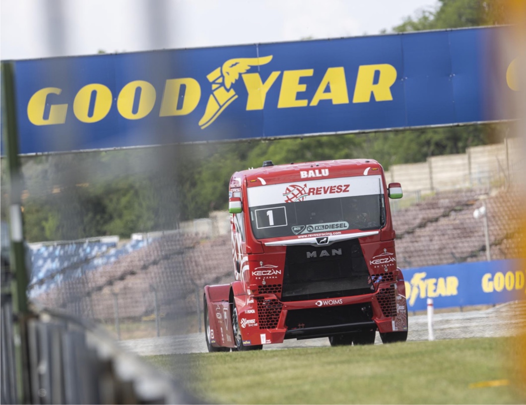Camión circulando en un circuito de carreras con una pancarta de Goodyear